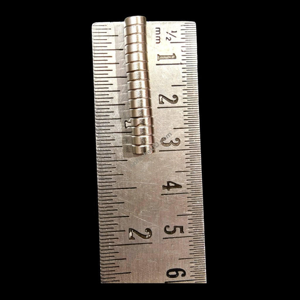 Stack of 5mm x 2mm neodymium disc magnets beside metric ruler on black background