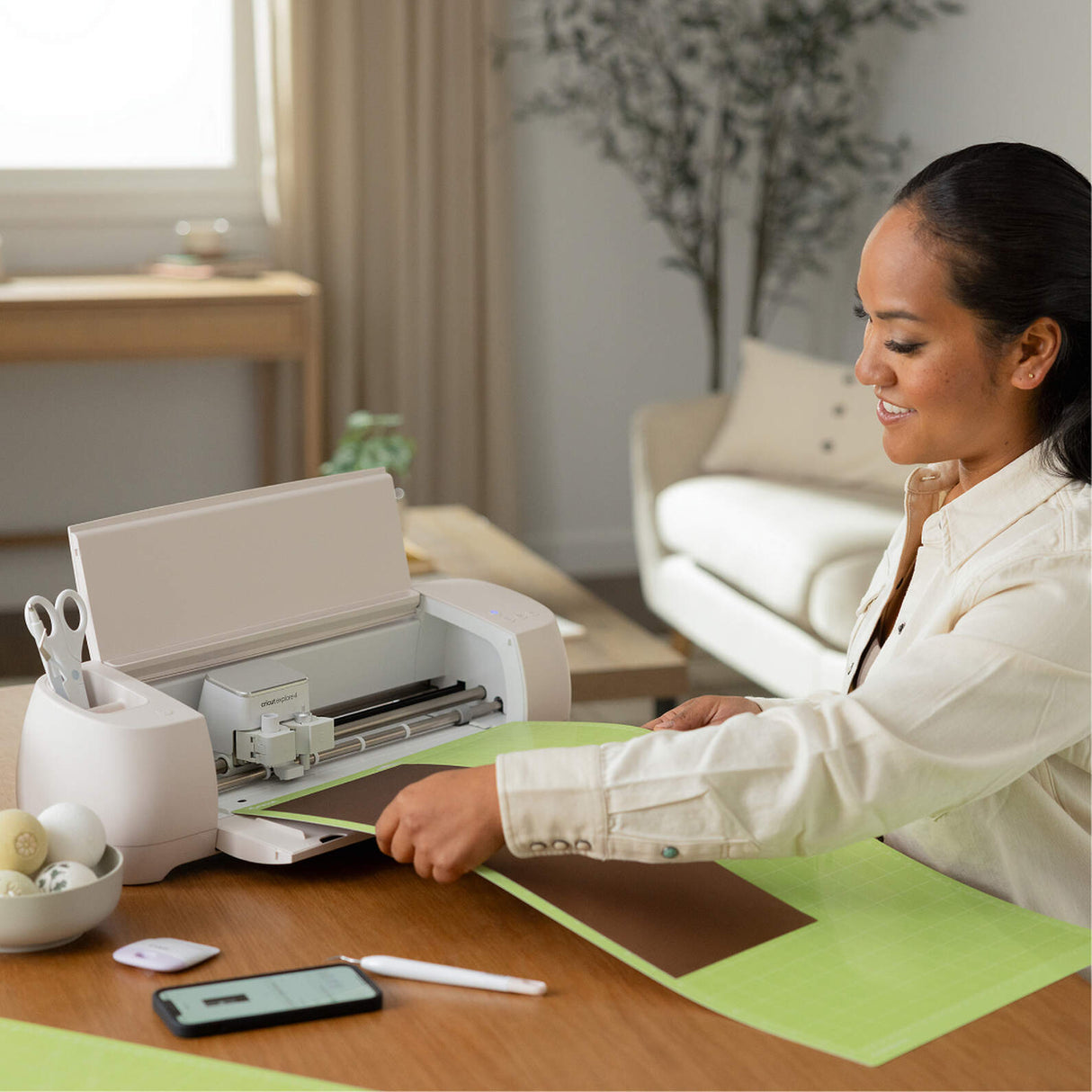 Woman loading brown cardstock on a green cutting mat into a white Cricut Joy 2 for DIY crafting.