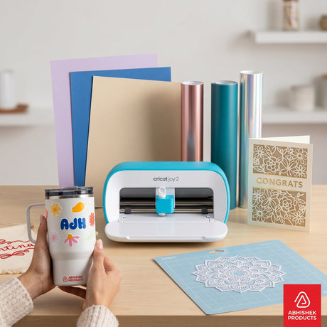 Blue Cricut Joy 2 cutting machine with vinyl rolls and cardstock, used for custom tumbler decals and card crafting.